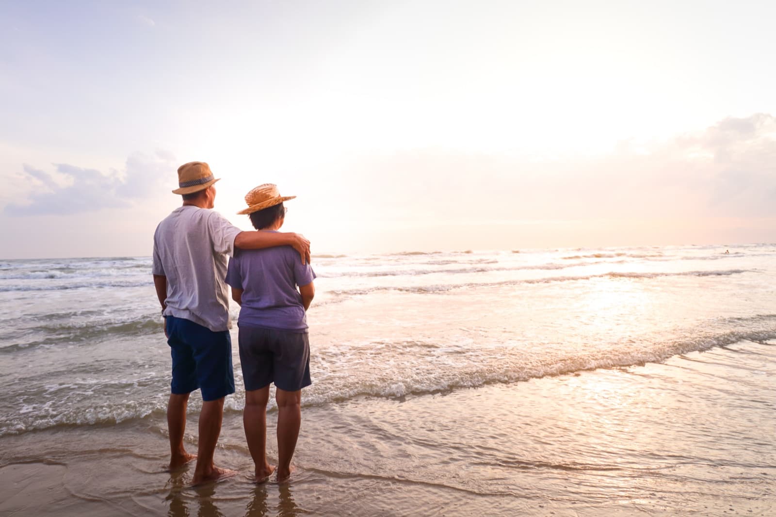 A senior couple standing together on the beach, looking out at the sea